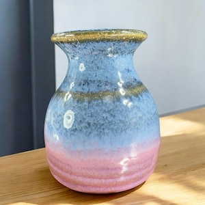 May include: A small, round ceramic vase with a light blue and pink glaze. The vase has a wide mouth and a narrow base.
