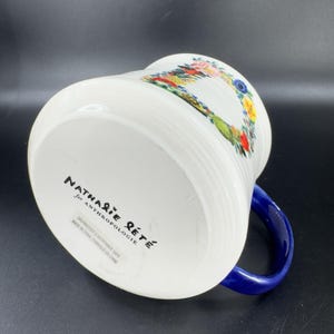 Puede incluir: Taza de cer&aacute;mica blanca con asa azul, con un dise&ntilde;o floral y de p&aacute;jaros. La taza tiene detalles acanalados verticales y el texto "Nathalie Lete for Anthropologie" est&aacute; impreso en la parte inferior.
