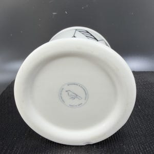 May include: White ceramic mug with a black graphic design and a bird logo on the bottom. The mug is labeled "Microwave & Dishwasher Safe" and "Made in China".