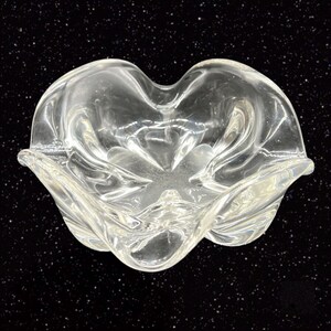 May include: A clear glass bowl with a wavy, organic shape. The bowl is designed with a ruffled edge and a slightly indented center.