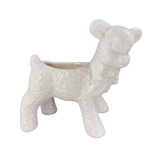 May include: A white ceramic planter shaped like a lamb with a pink glaze. The planter has a textured surface and a small opening on the top for planting.