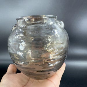 May include: A clear glass vase with a textured surface and two handles. The vase has a round body and a wide mouth.
