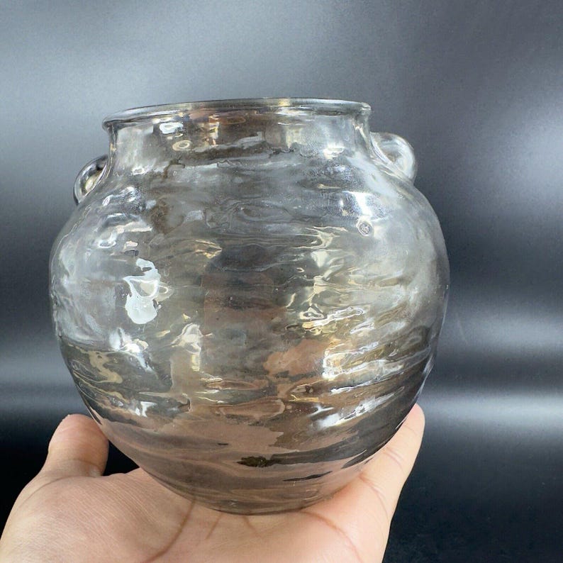 May include: A clear glass vase with a textured surface and two handles. The vase has a round body and a wide mouth.