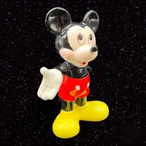Puede incluir: Una figurita de cer&aacute;mica de Mickey Mouse, un personaje de dibujos animados. Mickey lleva sus pantalones cortos rojos caracter&iacute;sticos con botones blancos y zapatos amarillos. Tiene orejas negras y una cara en blanco y negro con una gran sonrisa.