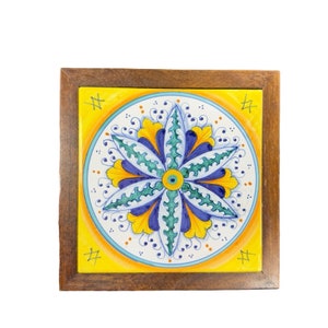 May include: A wooden framed tile with a yellow background and a blue, green, and yellow floral design.