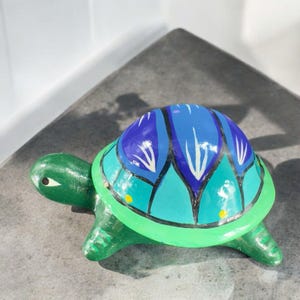 May include: A green turtle figurine with a blue and green shell. The shell has a decorative design with blue, green, and white accents.