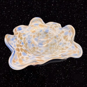 May include: A white glass bowl with blue and gold flecks. The bowl has a wavy, organic shape and is perfect for serving snacks or holding decorative items.