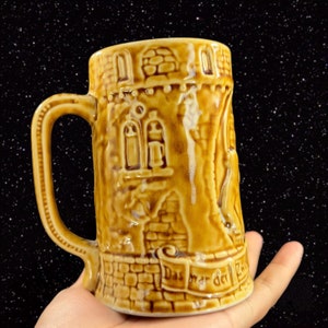 May include: A brown ceramic beer stein with a castle design and the text "Das war der 2. Weltkrieg" on the bottom.