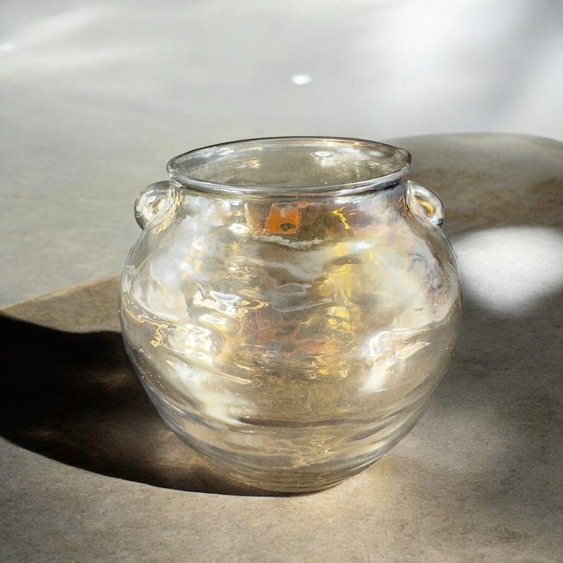May include: A clear glass vase with a gold iridescent finish and two small handles. The vase has a round body and a slightly flared opening.