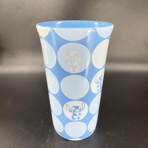 May include: A blue ceramic mug with a white polka dot pattern and a white silhouette of Stitch from Lilo & Stitch on each dot.