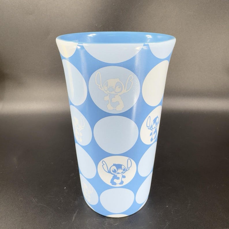 May include: A blue ceramic mug with a white polka dot pattern and a white silhouette of Stitch from Lilo & Stitch on each dot.