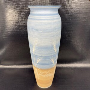 May include: Tall ceramic vase with a light blue and tan color scheme. The vase features a wheat design in white. The vase is approximately 12 inches tall.