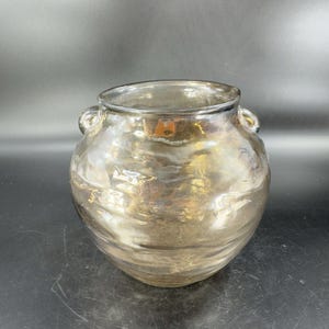 May include: A clear glass vase with a textured, iridescent finish. The vase has two small handles on the sides and a rounded body.