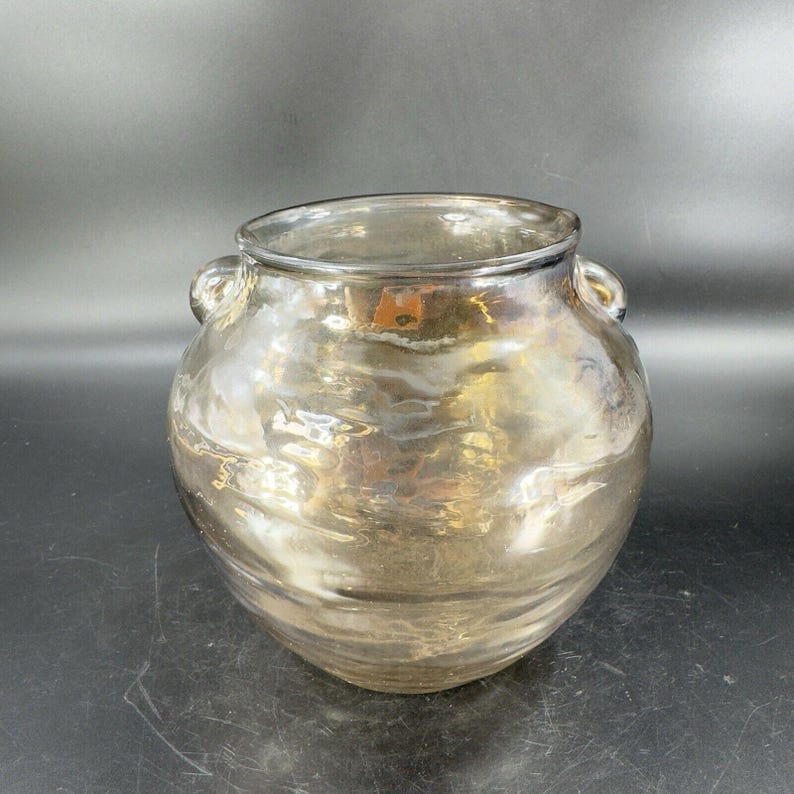 May include: A clear glass vase with a textured, iridescent finish. The vase has two small handles on the sides and a rounded body.