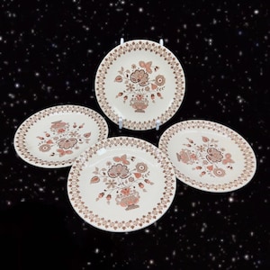May include: Set of four white ceramic dinner plates with a brown and orange floral pattern. The plates have a scalloped edge and a delicate floral design.