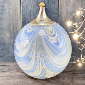 May include: A round, glass oil lamp with a blue and white swirled pattern. The lamp has a silver-colored metal top and a wick. The background is a weathered, gray wooden surface.