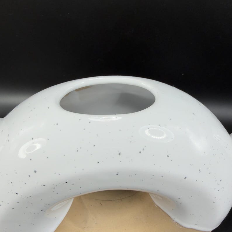 Peut inclure: Un vase en c&eacute;ramique blanc avec un motif tachet&eacute;. Le vase a une forme arrondie unique avec une grande ouverture en haut. L'int&eacute;rieur est de couleur beige clair, contrastant avec l'ext&eacute;rieur blanc. Le vase est un objet d&eacute;coratif.
