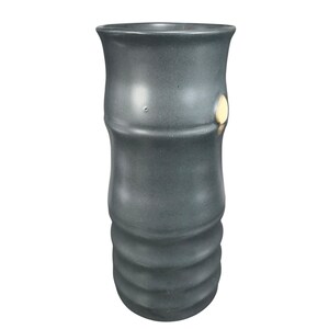 May include: A dark gray ceramic vase with a bamboo-like design. The vase has a cylindrical shape with a flared top and a series of horizontal ridges near the base. A small, light-colored patch is visible on the side.