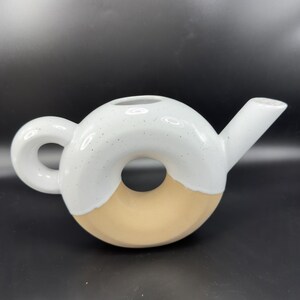 Peut inclure: Une th&eacute;i&egrave;re en c&eacute;ramique de forme originale en donut. La moiti&eacute; sup&eacute;rieure est blanche avec des d&eacute;tails mouchet&eacute;s, la moiti&eacute; inf&eacute;rieure est beige clair. Elle poss&egrave;de une anse arrondie et un bec verseur, id&eacute;ale pour le th&eacute;.