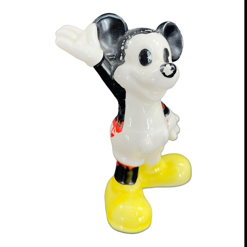 K&ouml;nnte beinhalten: Eine wei&szlig;e Keramikfigur von Mickey Mouse mit schwarzen Ohren und Schuhen. Mickey tr&auml;gt rote Shorts und hat ein schwarz-wei&szlig;es Farbspritzer-Design auf seinem K&ouml;rper. Er winkt mit der rechten Hand und hat einen freundlichen Gesichtsausdruck.