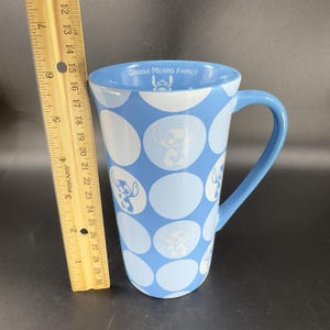 May include: A blue ceramic mug with a white polka dot pattern and a blue handle. The mug features a cartoon character with the text "Ohana Means Family" on the top.