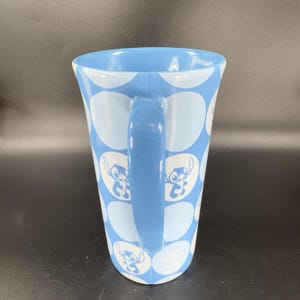 May include: A blue ceramic mug with a white polka dot pattern and a blue handle. The mug features a cartoon character, Stitch, from the Disney movie Lilo & Stitch.