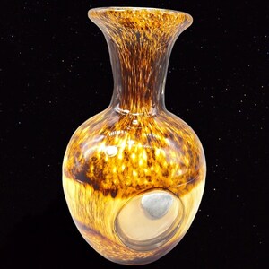 May include: A brown and gold glass vase with a round body and a thin neck. The vase has a large, circular opening in the side.