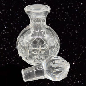 May include: A clear glass bottle with a textured, faceted design. The bottle has a separate stopper with a pointed top.