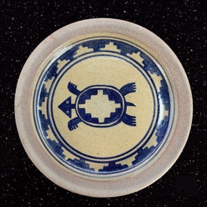 May include: A ceramic plate with a blue and white turtle design. The turtle is stylized and has a geometric pattern on its shell. The plate has a beige rim.