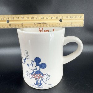 May include: White ceramic coffee mug with a cartoon image of Mickey Mouse and Minnie Mouse. The mug has the text "I'm tum!" printed on it.