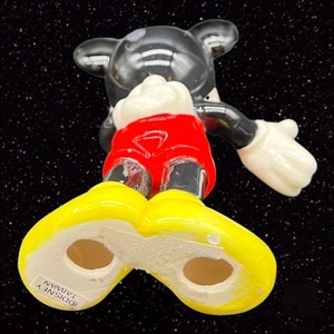 Puede incluir: Una figurita de cer&aacute;mica de Mickey Mouse con pantalones cortos rojos y zapatos amarillos. La figurita est&aacute; de pie con los brazos extendidos. La figurita est&aacute; hecha en Taiw&aacute;n y tiene el copyright de Disney en la parte inferior del zapato.