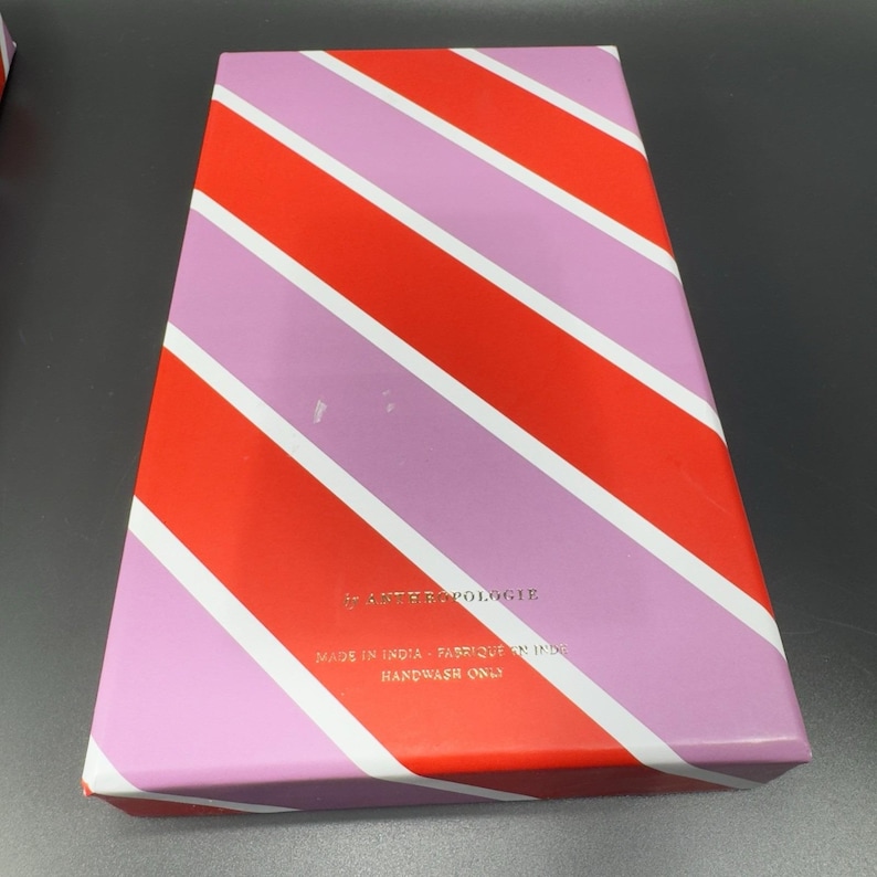 May include: A rectangular box with a diagonal striped pattern in red, pink, and white. The box has the word "Anthropologie" printed on it, along with the text "Made in India - Fabriqu&eacute; en Inde" and "Handwash Only".