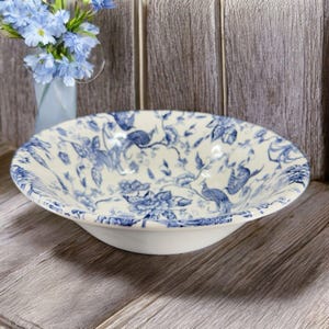 May include: A white ceramic bowl with a blue and white floral pattern. The bowl is decorated with a repeating pattern of birds and flowers.