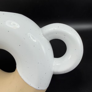 Peut inclure: Gros plan sur une tasse en c&eacute;ramique blanche avec une anse arrondie. La tasse pr&eacute;sente un motif mouchet&eacute; et une finition lisse et brillante. La anse est de forme circulaire et la tasse semble vide.