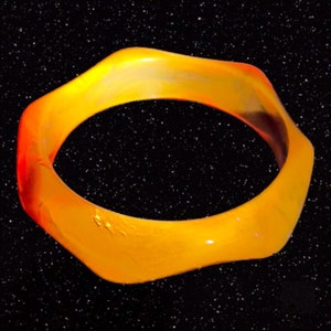 May include: A bright orange, glossy, ring-shaped object with a smooth, rounded surface. The object is set against a black background with white specks.