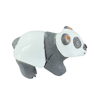 May include: A ceramic panda figurine with a white body, black legs, and a black and white head. The panda has small, round ears and a detailed face with black eye patches and a small nose. The figurine is a decorative item.
