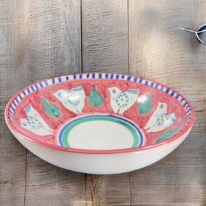 May include: A large, white ceramic bowl with a pink rim and a green and white design of birds and cacti. The bowl is perfect for serving salads, pasta, or fruit.