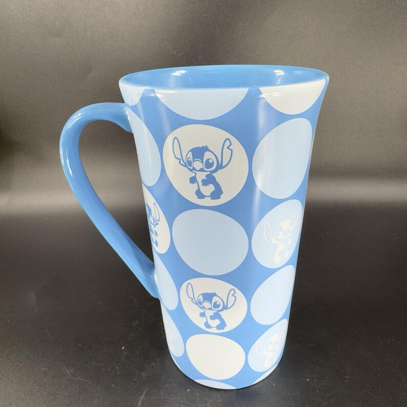 May include: A blue ceramic mug with a white polka dot pattern and a silhouette of Stitch from Lilo & Stitch on each dot.
