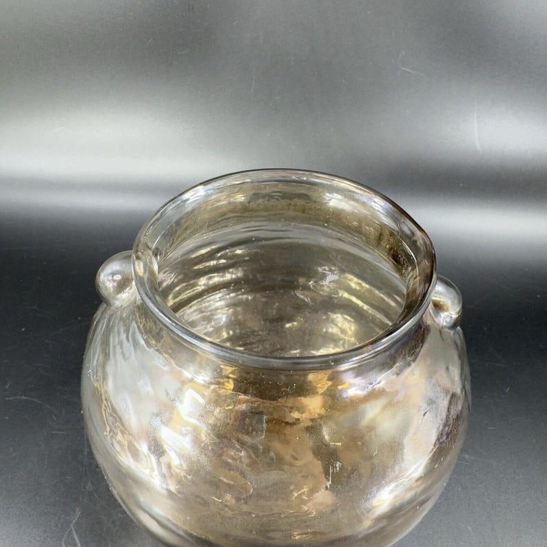 May include: A clear glass vase with a round body and two small handles. The vase has a metallic, iridescent finish.