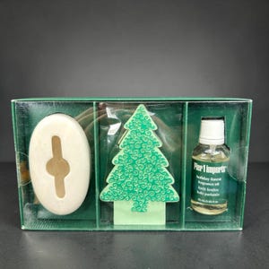 May include: A Pier 1 Imports holiday forest fragrance oil set. The set includes a white oval-shaped soap, a green Christmas tree-shaped air freshener, and a small bottle of fragrance oil. The packaging is a clear plastic box with a green base.