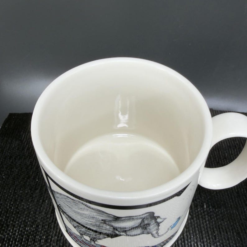 May include: White ceramic mug with a wraparound illustration. The illustration features a detailed black and white drawing with blue and red accents. The mug has a curved handle and a glossy finish.