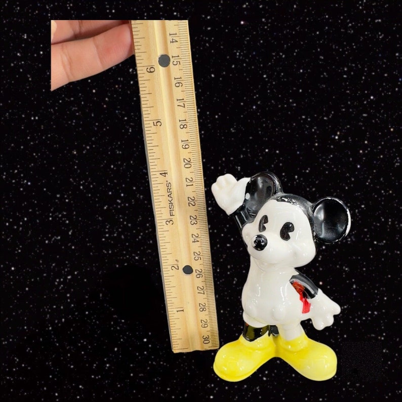 K&ouml;nnte beinhalten: Eine schwarze und wei&szlig;e Keramikfigur von Mickey Mouse, die mit erhobenem rechten Arm steht und gelbe Schuhe tr&auml;gt. Die Figur ist etwa 15 cm gro&szlig;.