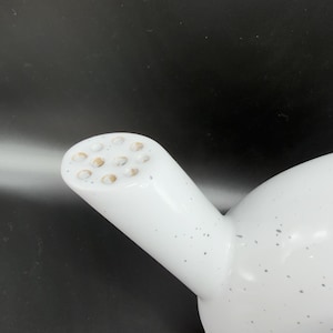 Peut inclure: Th&eacute;i&egrave;re en c&eacute;ramique blanche avec un bec verseur &agrave; plusieurs trous. La th&eacute;i&egrave;re pr&eacute;sente un motif mouchet&eacute; avec de petits points gris. Le bec verseur est cylindrique et inclin&eacute;, avec un corps arrondi. Le fond est sombre.