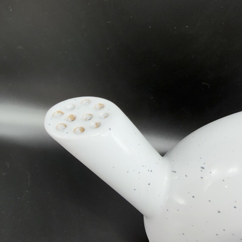 Peut inclure: Th&eacute;i&egrave;re en c&eacute;ramique blanche avec un bec verseur &agrave; plusieurs trous. La th&eacute;i&egrave;re pr&eacute;sente un motif mouchet&eacute; avec de petits points gris. Le bec verseur est cylindrique et inclin&eacute;, avec un corps arrondi. Le fond est sombre.