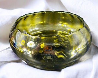 May include: A green glass bowl with a wavy, rippled design. The bowl is empty and has a reflective surface.