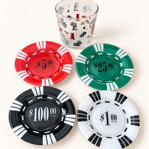 May include: A clear glass tumbler decorated with black and red game icons, accompanied by four round glass coasters designed like poker chips. The coasters are red with $5.00, green with $25.00, black with $100.00, and white with $1.00 printed on them.