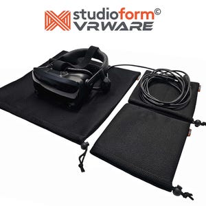 Op de afbeelding: Drie zwarte mesh trekkoordtassen met een VR-headset en kabel erin. De tassen zijn gelabeld "studioform VRWARE".