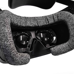 May include: Close-up of a black virtual reality headset with a gray fabric face cushion. The headset has two lenses for each eye.