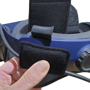 Op de afbeelding: Een close-up van een blauwe virtual reality headset met een zwarte band en een zwart stoffen kussen. De headset heeft een zwarte kabel.
