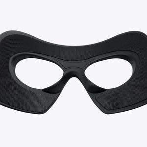 May include: Black eye mask with a textured surface and oval eye openings. The mask has a curved design and is likely for costume or sleep purposes. The mask is made of a soft, flexible material.